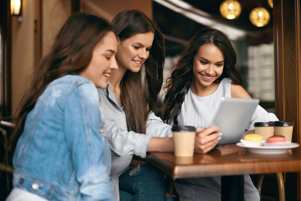 Friends happily watching a laptop screen while sitting outdoors at a cafe.