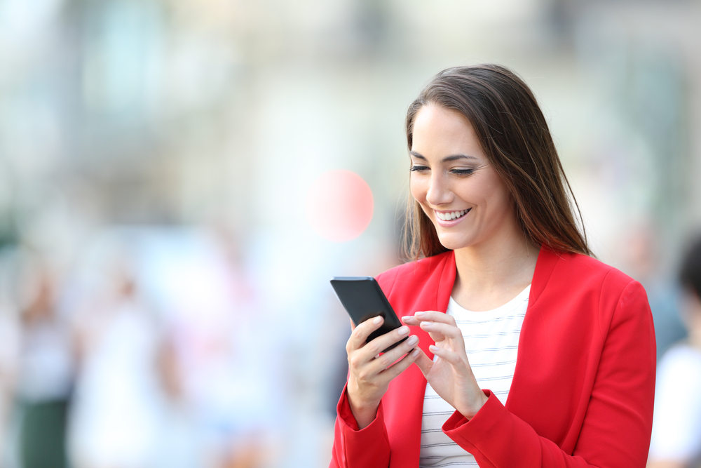 A woman looks happy to be browsing on her phone while outside.